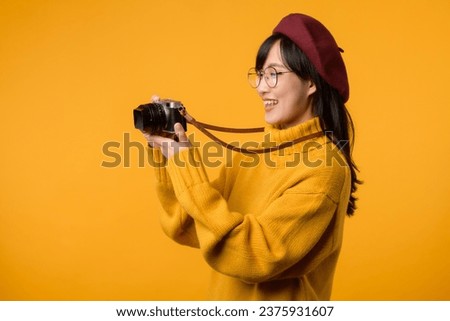With her trusty camera in hand, young Asian woman explores the world, embodying the spirit of a photographer in her stylish yellow sweater and red beret.