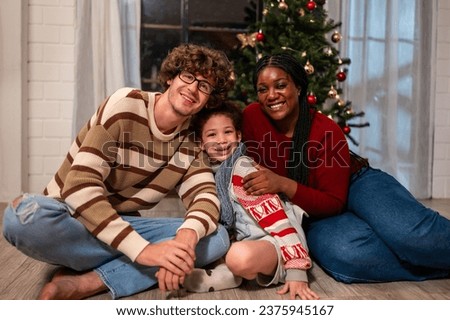Portrait of Multi-ethnic family celebrate Christmas party in house.  Attractive young parents sit with little kid daughter enjoy celebrating holiday Christmas, Thanksgiving and looking at camera.