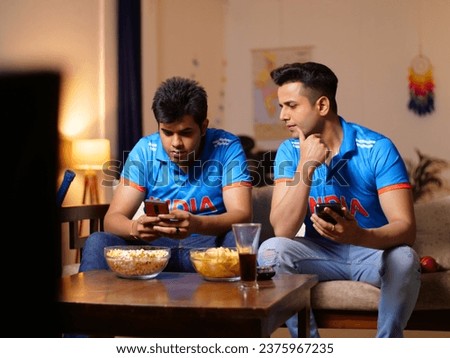 Two young brothers checking the live cricket score - placing online bets, Indian cricket teams, sports app, online gaming addiction . Indian men watching online live cricket match on an app