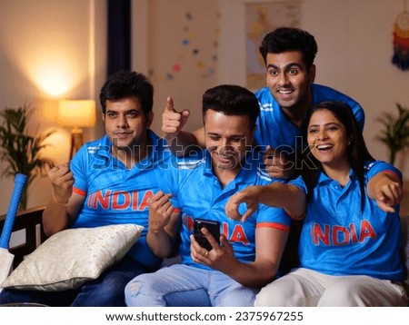Group of friends happily enjoying the live cricket match on television at home - wearing an Indian cricket jersey, women fan, fans. Siblings gathered around a large-screen television - watching TV