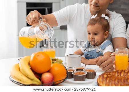 Dad pours a glass of orange juice for his cute little daughter during breakfast. Selective focus. Family breakfast concept. 