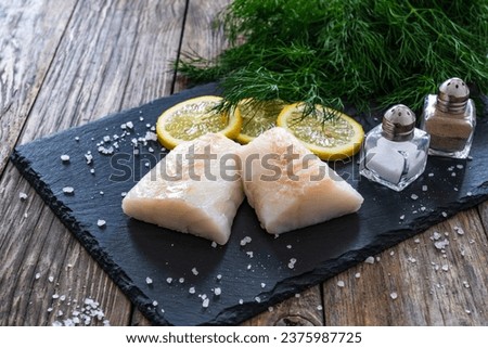 Fresh raw cod with lemon and dill on cutting board on wooden table 