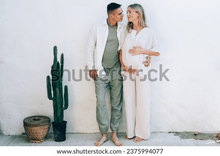 A married pregnant couple stands against a white wall. Tender love relationship of a man and a woman