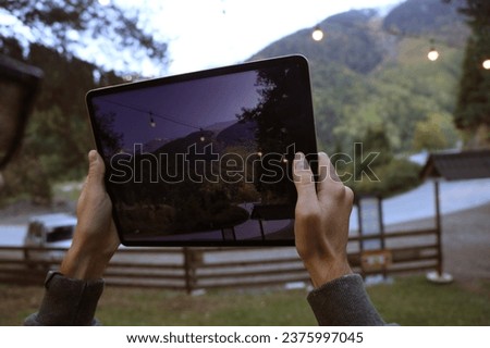 male Hands holding big modern tablet and taking photo of a autumn mountains landscape. man working with device, tablet computer and mobile smart phone. no face. unrecognizable person. asphalt road