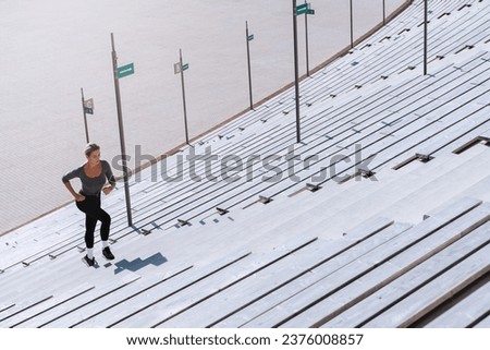 Woman athlete wearing female sportswear running and  exercising on staircase between bleachers of outdoor stadium. Royalty-Free Stock Photo #2376008857