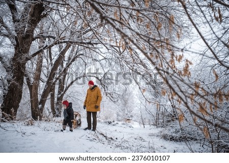 little boy 2-3 years old and his father are playing in the snow, the child is sledding and pulling sled made of wicker in snow. Parental involvement in raising children. Winter fun and relaxation