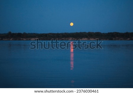 Natural landscape with night sky and yellow moon reflected in water in the river. Soothing picture of tranquil nature. Perfect night scene.