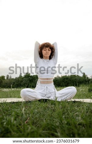 Concept of pranayama. Young sportive woman spend her free time on fresh air meditation. Girl closed eyes folded hands behind back. Sports aerobics coach demonstrate asana pose in park