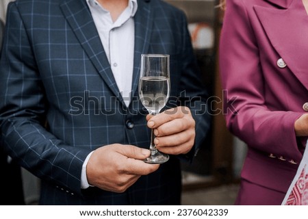 A stylish man in a blue checkered jacket holds a glass of champagne, wine in his hands at a banquet, party. Food photography.