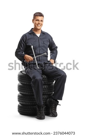 Car mechanic sitting on a pile of tires and holding a wrench tool isolated on white background Royalty-Free Stock Photo #2376044073