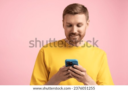 Man with phone, studio portrait. Smiling happy glad guy isolated on pink uses smartphone, typing message, texting, chatting, communicating in instant messengers online, Internet social media networks. Royalty-Free Stock Photo #2376051255