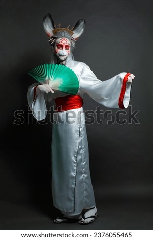 Portrait of beautiful woman in animal mask and white kimono standing on black background. Halloween, Carnival and Cosplay concept