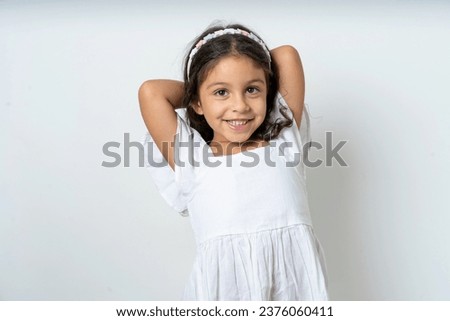 Satisfied beautiful kid girl wearing white dress hold hands behind head relaxing