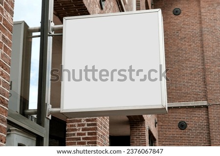 Square blank light box hanging on a brick wall in a street for use a template or mock-up