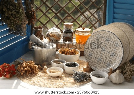 Many different dry herbs, flowers and plates on white wooden table near window
