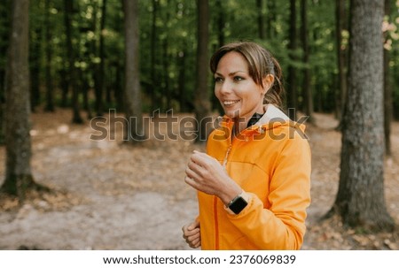 A photo of a beautiful young woman running in the park using smartwatch. Fresh air at forest. A healthy lifestyle