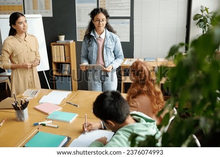 Clever schoolgirl in denim casualwear explaining new grammar rules to classmates during presentation while standing next to teacher