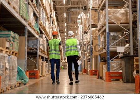 two men in warehouse wearing safety helmet, vest. Concept for industry, job, meeting, work training. Two Caucasian warehouse workers walking in distribution storage area discussing Royalty-Free Stock Photo #2376085469
