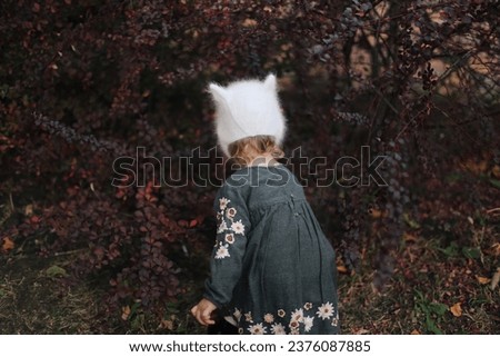 Adorable babygirl in a kitten hat looking for treasures in the autumn forest 