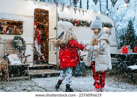 children siblings boy and girls in pajamas and jackets having fun near trailer mobile home or recreational vehicle during winter family local travel on Christmas and New Year, waiting for snowfall 