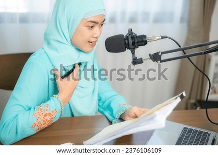 A young smiling muslim female wearing headphones with a microphone while recording podcast at home