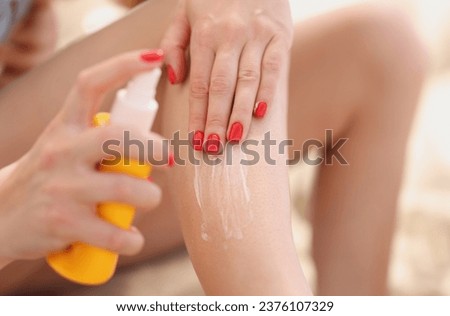 Close-up of female applying sunscreen lotion on legs, female with red manicure, protect body from sun. Cosmetology, aging prevention, beach day concept