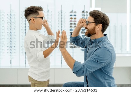 Portrait of happy attractive father and choosing and buying eyeglasses giving five high in optical store. Health care, vision concept  Royalty-Free Stock Photo #2376114631