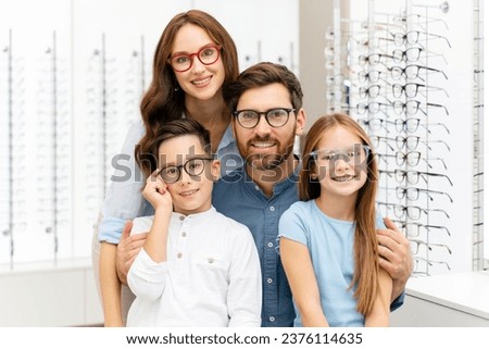 Portrait of young smiling family hugging choosing stylish glasses in modern optical store. Vision concept  Royalty-Free Stock Photo #2376114635