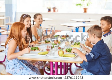 Happy kids having meal with cutlery while sitting together at table in school canteen Royalty-Free Stock Photo #2376119243