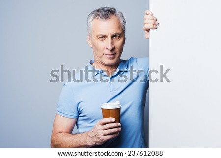 Keep calm and drink coffee. Handsome senior man holding cup of coffee and leaning at copy space while standing against grey background