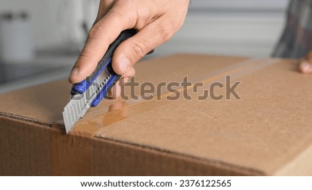 Male person hold clerical knife. Man cut mail box close up. Guy open new parcel. Hands unpacking postal package. Young adult unboxing e-commerce box. Client buy carton gift. Receiver unzip post pack. Royalty-Free Stock Photo #2376122565