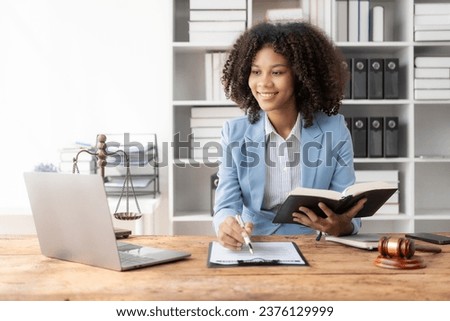 Attractive young African American lawyer working in the office with contract and legal documents when sitting at the table. Law, legal services, advice, justice. Royalty-Free Stock Photo #2376129999