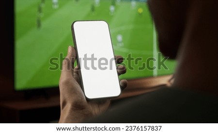 CU Black African-American male watching soccer at home, making bets on his phone. Online betting, sports bookmaker. Phone mockup Royalty-Free Stock Photo #2376157837