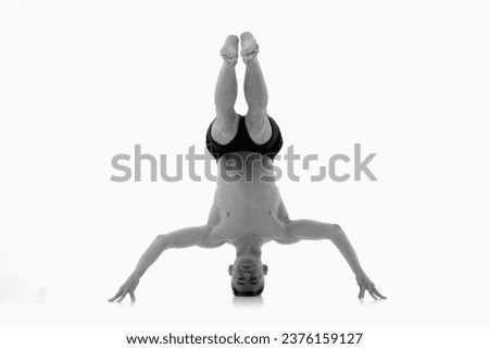 Headstand yoga asana, Ashtanga yoga  Side view of man wearing sportswear doing Yoga exercise against white background.  Black and white image. Royalty-Free Stock Photo #2376159127