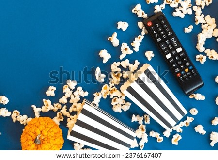 Popcorn and decorative pumpkins with TV remote on a blue background with copy space. Movie night concept. Wateching TV themed photo. Fall or autumn TV shows.