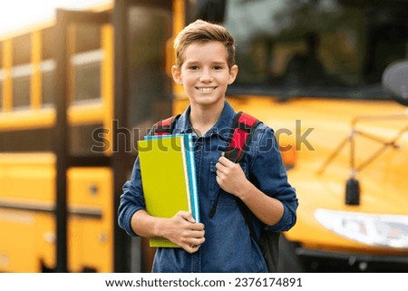 Back To School. Happy smiling preteen boy standing near school bus with backpack and workbooks in hands, cheerful male kid posing outdoors while going to classes, pupil child enjoying study Royalty-Free Stock Photo #2376174891