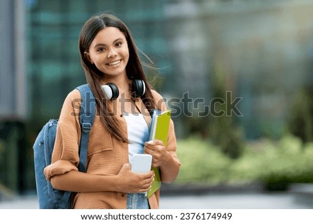 Smiling student holding books, posing at college campus. Radiant pretty young woman holding books, standing at university, symbolizing a blend of joy and scholarly pursuits, copy space Royalty-Free Stock Photo #2376174949
