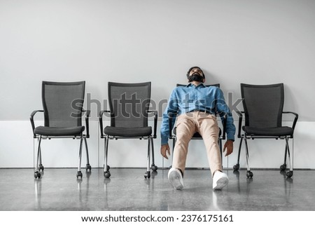Bored and disappointed male indian employee sitting in waiting room on row of chairs, feeling tired and upset, full length shot, free space Royalty-Free Stock Photo #2376175161