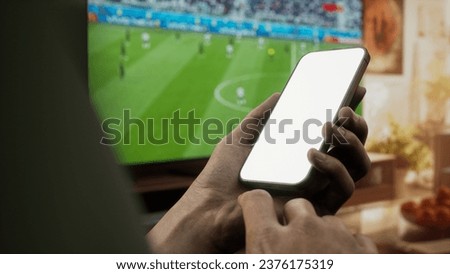 CU Black African-American male watching soccer at home, making bets on his phone. Online betting, sports bookmaker. Phone mockup Royalty-Free Stock Photo #2376175319