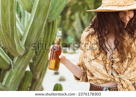 Carefree girl enjoying beer in the Mexican desert, surrounded by cacti. Smiling young woman holding a bottle of beer, relaxing during vacation in South America. Brown toning picture.