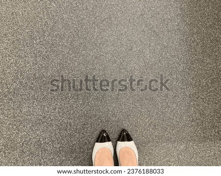 Asphalt concrete floor texture and a peek of women’s stylish chanel black tipped and grey shoes. copy space.negative space.