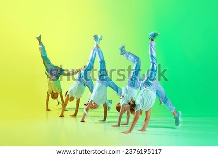 Group of little cute flexible girls dressed in fashion, stylish outfit dancing in choreography class isolated on green-yellow gradient background in neon light. Concept of hobby, music, motion. ad