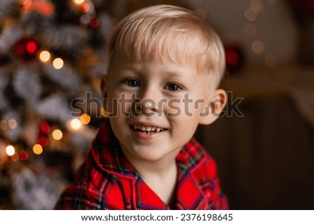 Portrait of a smiling blond boy in a red sweater against the background of Christmas lights