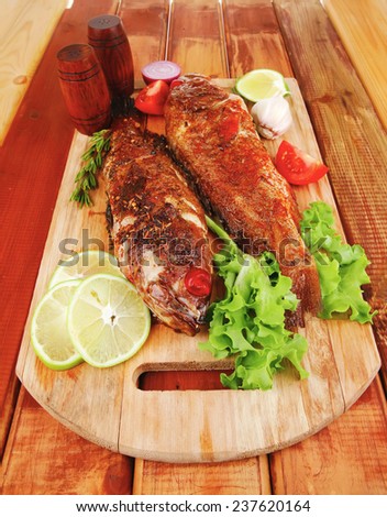 roasted sea fish and castors on wood with tomatoes, lemon and green lettuce salad
