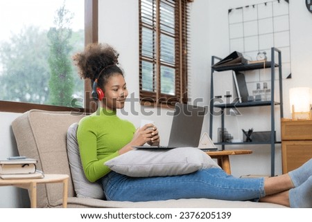 Young woman with IT idea of ​​African American descent wearing a green t-shirt sitting on a sofa chair working on a laptop computer at home, relaxing, simple style, relaxing.