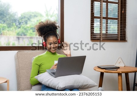 Young woman with IT idea of ​​African American descent wearing a green t-shirt sitting on a sofa chair working on a laptop computer at home, relaxing, simple style, relaxing.
