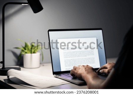 Man writing text document, essay or letter with laptop. Freelance writer, journalist or entrepreneur working late at night, overtime. Job seeker, cv resume and application. Dark home or office room. Royalty-Free Stock Photo #2376208001