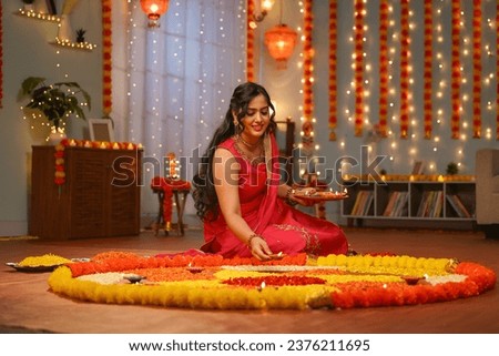 Happy young Indian woman placing diya lamps on decorated flower rangoli for diwali festival celebration at home - concept of festive preparation, traditional culture and spirituality Royalty-Free Stock Photo #2376211695