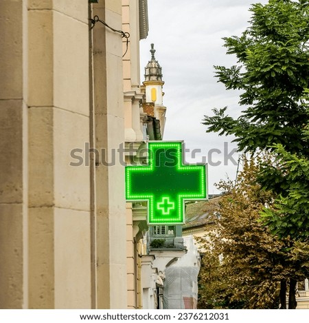 Green shining medical cross indicating the location of a pharmacy on street. Green Cross on a Building, sign of pharmacy