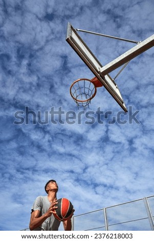 Low angle of male basketball player looking at ring and preparing to throw ball into basket against summertime